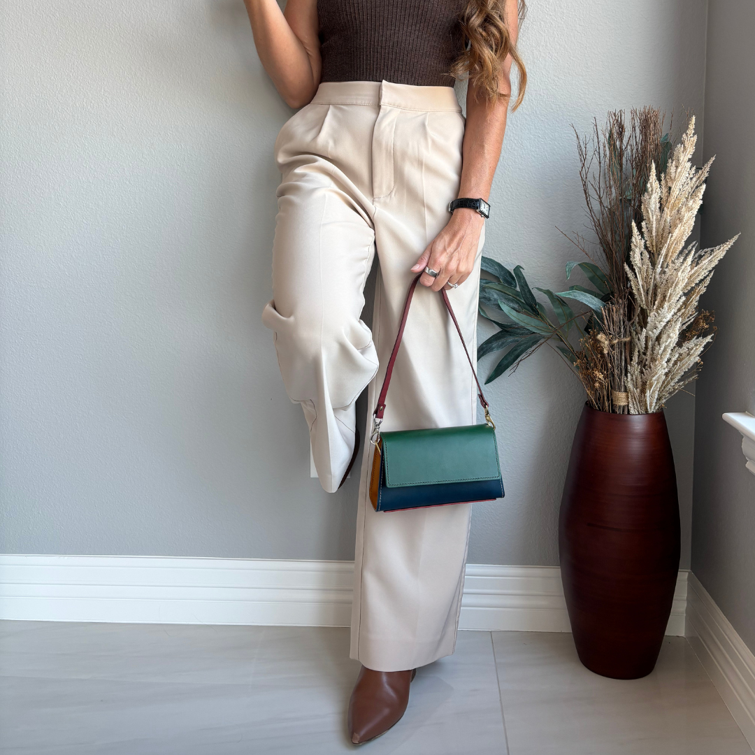 The Wild Card 2026 handcrafted leather shoulder bag carried by hand with a neutral outfit, showing its green and navy leather exterior.